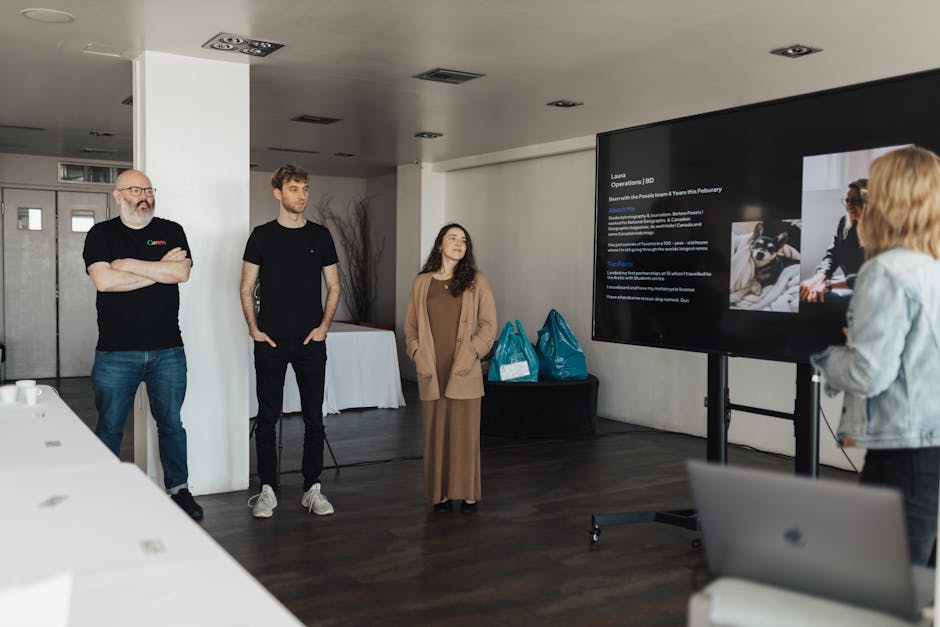 Professionals attending a business presentation in a contemporary office setting with a large screen display.