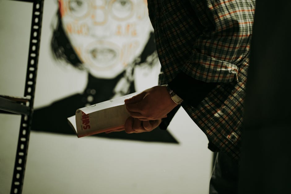A person holding a book in an art gallery featuring modern artwork on a wall.